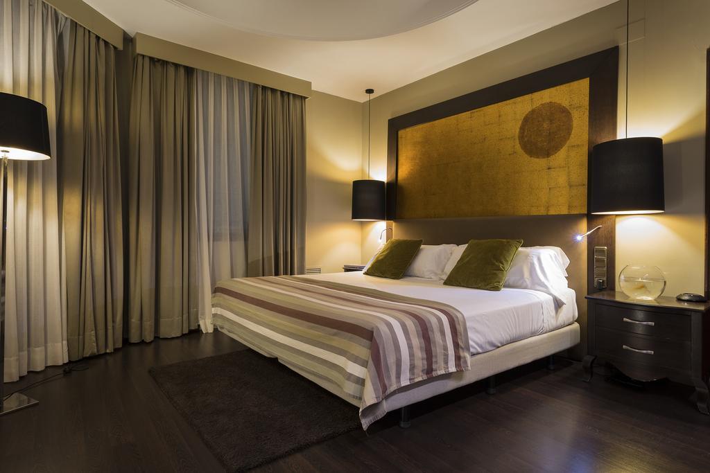 Only You Hotel Valencia Bagian luar foto The photo shows a modern bedroom that features a large bed with two green accent pillows and a striped bedspread. The room has a warm, neutral color scheme, highlighted by soft lighting from two bedside lamps. The wall behind the bed has an artistic 